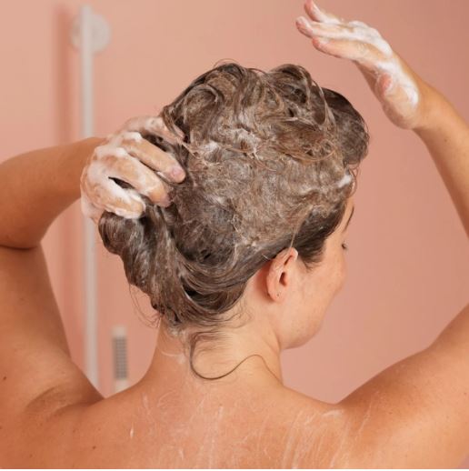 Frau wäscht Haar mit ReNu Smoothing Shampoo von Nu Skin
