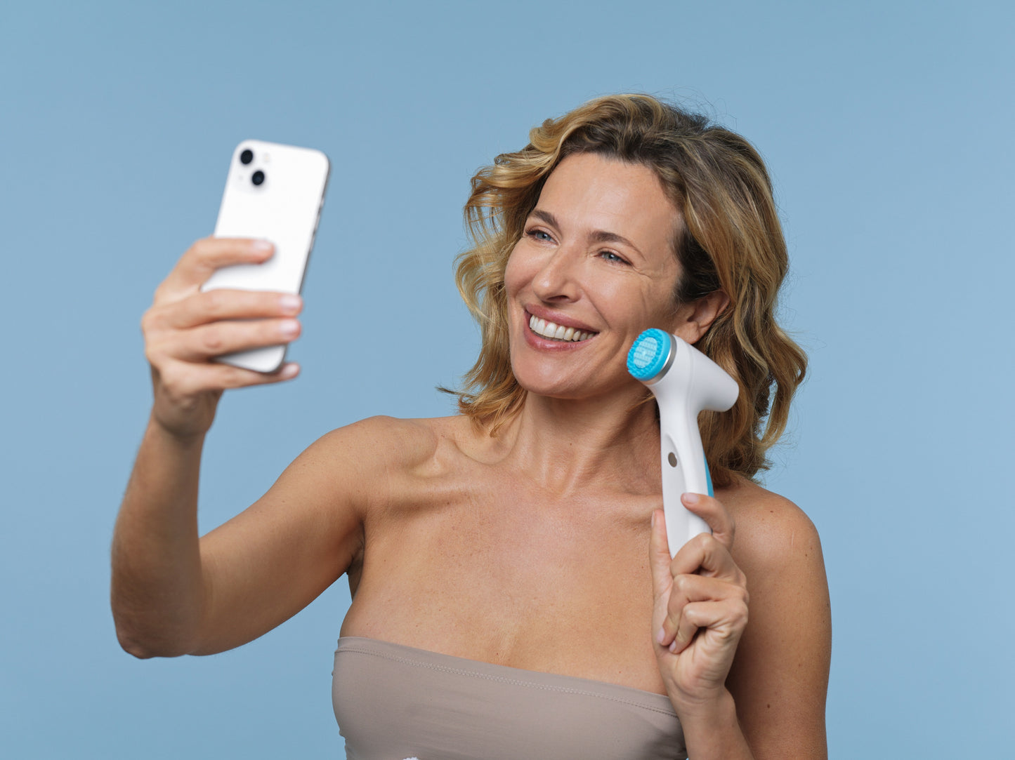 Customer holds LumiSpa iO and cell phone LumiSpa iO you can connect via Blutetooth with the Nu Skin Vera app on your cell phone to help you reach your grooming goals with intelligent IoT-technology (Internet of Things).