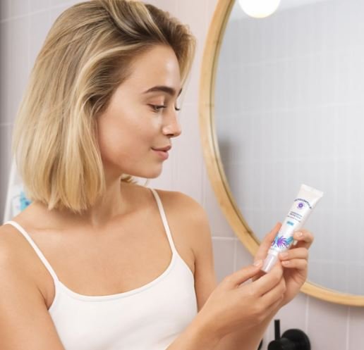 Vrouw staat voor een spiegel met een tube Complexion Protection Mineral Sunscreen met SPF 50